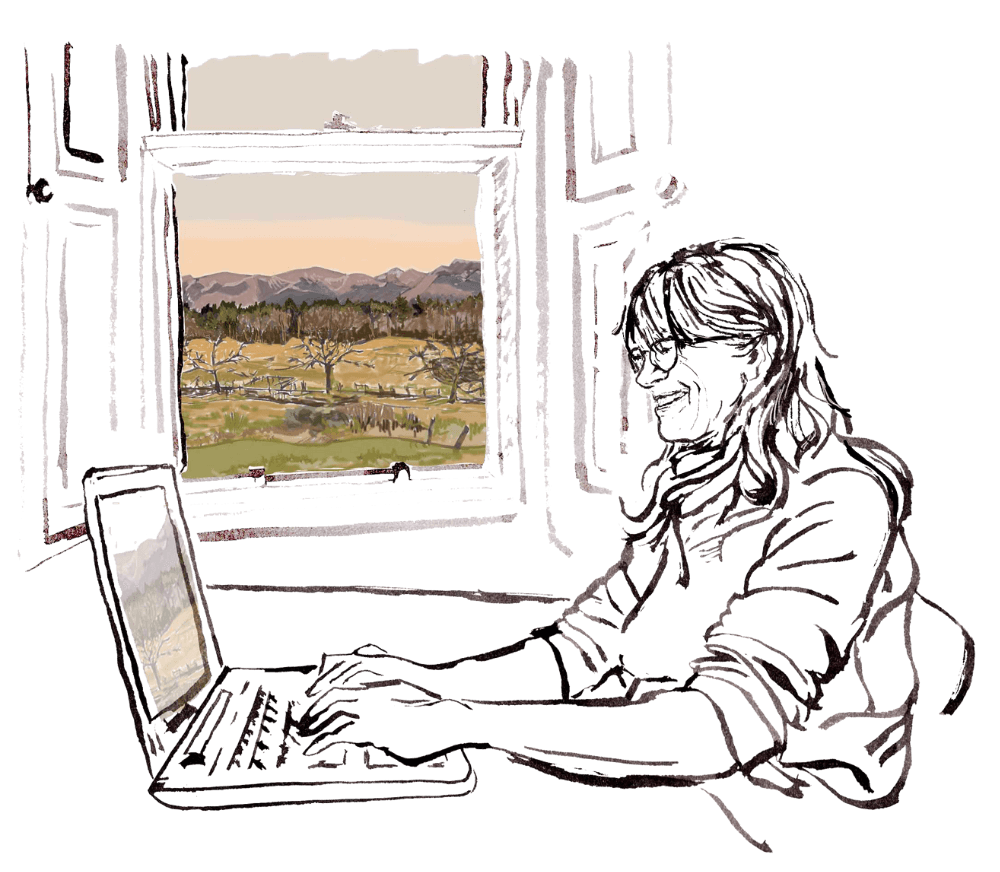 Image of Julia Lister happily working at a laptop in front of a window through which you can see a view of the Cairngorm mountains.